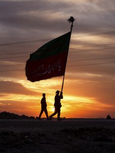 دو زائر که پرچم بزرگی در دست دارند هنگام طلوع پیاده‌روی می‌کنند.