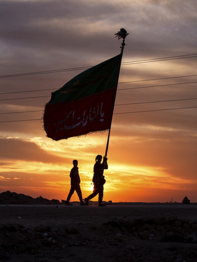 دو زائر که پرچم بزرگی در دست دارند هنگام طلوع پیاده‌روی می‌کنند.