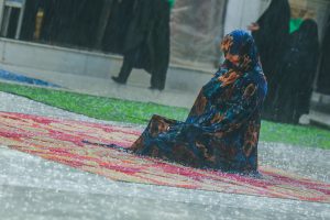 زائری در حرم امیرالمؤمنین زیر بارش باران نشسته