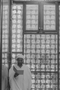 یک زائر در حال خواندن زیارت مقابل پنجره مشبک ایوان