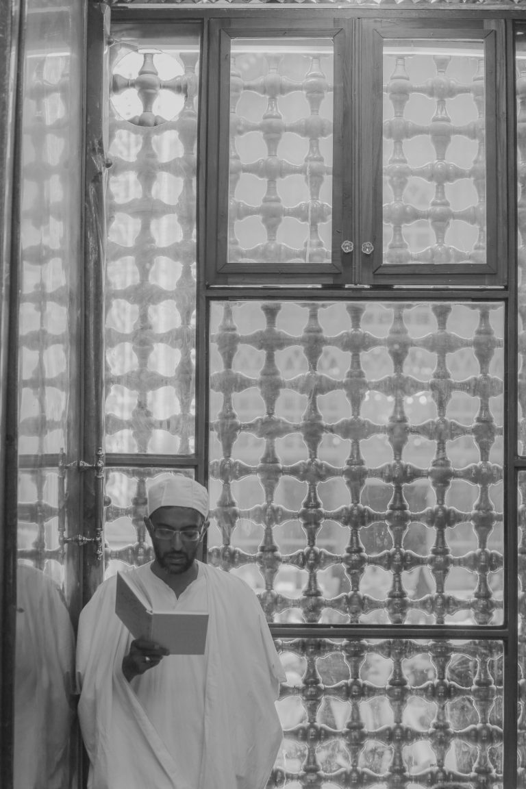 یک زائر در حال خواندن زیارت مقابل پنجره مشبک ایوان