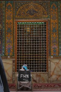 یک زائر روی ویلچر در مقابل پنجره مشبک ایوان ناودان طلا