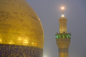 گلدسته در دوردست و گنبد حرم امیرالمؤمنین در مه صبحگاهی