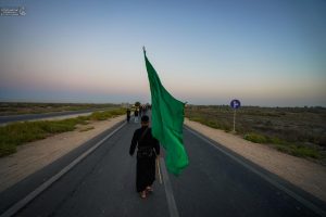 زائری با پرچم سبز در جاده پیاده می‌رود