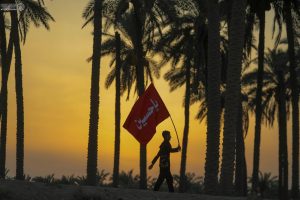 یک زائر جوان با پرچم یا حسین در پیاده‌روی اربعین