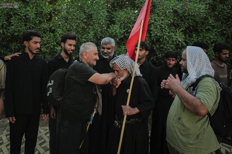 خادم حسینی در حال بوسیدن دست زائر