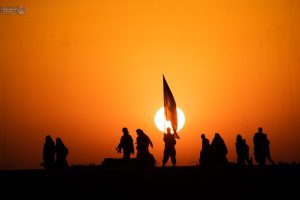 سایه مردان و پرچم و غروب آفتاب در پشت آنها در مسیر پیاده‌روی