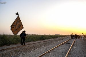 زائری با پرچم الحسین طریق التائبین در کنار ریل راه آهن