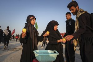 دختران به زائران سیب می‌دهند