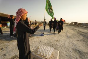 پسری در حال تقدیم آب به زوار اربعین