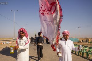 دو خادم عراقی موکب با لیوان آب در انتظار زائران پیاده‌روی اربعین