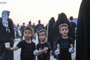 چهار کودک در حال تقدیم آب آشامیدنی به زوار پیاده اربعینی