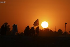 خورشید غروب پشت پرچم و زائران اربعین