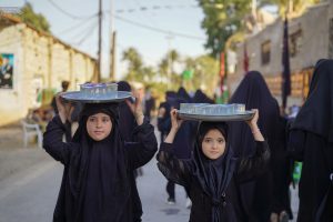 دو کودک در حال حمل سینی پذیرایی برای زائران