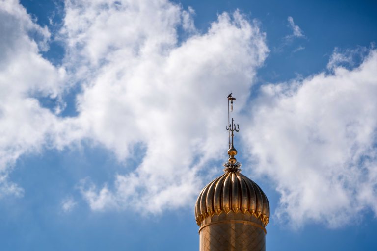 نمای نزدیک نماد تزئینی گلدسته طلایی حرم امیرالمؤمنین در آسمان ابری