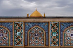 نمایی از کاشی‌کاری‌های هندسی حرم علوی با گنبد طلایی در پس‌زمینه