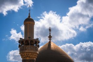 نمای نزدیک گلدسته و گنبد طلایی حرم علوی و آسمان ابری