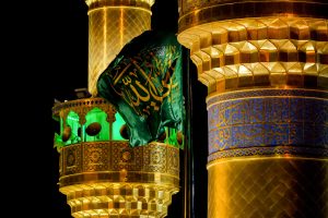 مای نزدیک گلدسته‌های حرم مطهر امیرالمؤمنین و پرچم علی ولی الله