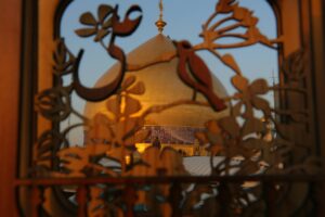 نقش نام علی و گل و تزئینات صحن با پس‌زمینه گنبد مطهر حرم