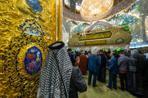زائری ایستاده کنار در و ضریح به همراه تزئینات عید در پس‌زمینه