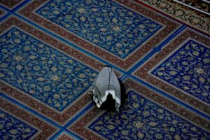 مردی با لباس سنتی عربی نشسته بر فرش‌های صحن از نمای بالا