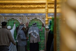 چند زائر در حال زیارت ضریح در فضای داخلی مرقد امیرالمؤمنین
