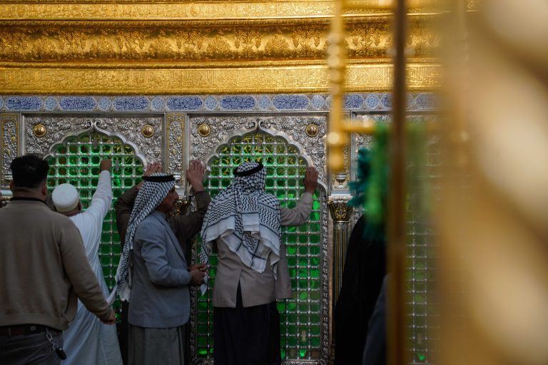 چند زائر در حال زیارت ضریح در فضای داخلی مرقد امیرالمؤمنین