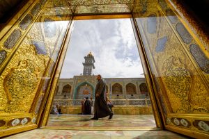 نمای صحن حرم امیرالمؤمنین علی (علیه‌السلام) از میان درِ طلایی، با زائری در ایوان
